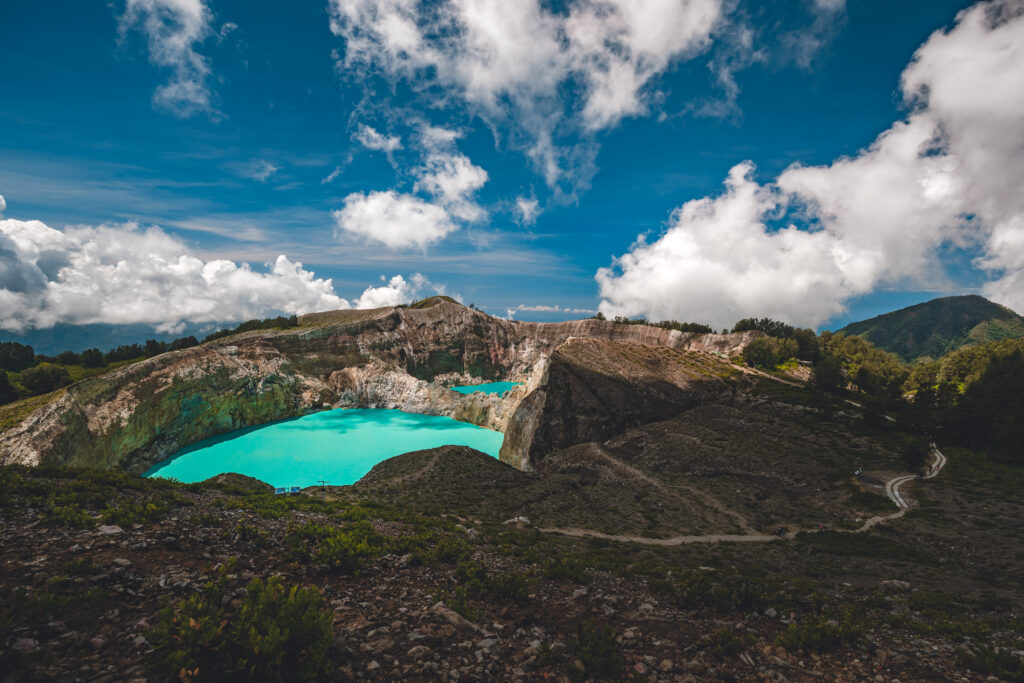 Indonesia volcano rocks crater lakes on green mountain Kelimutu peak with clear turquoise water. Indonesian Flores island, Asia landmark with landscape at cloudy sky. Cinematic volcanic scene